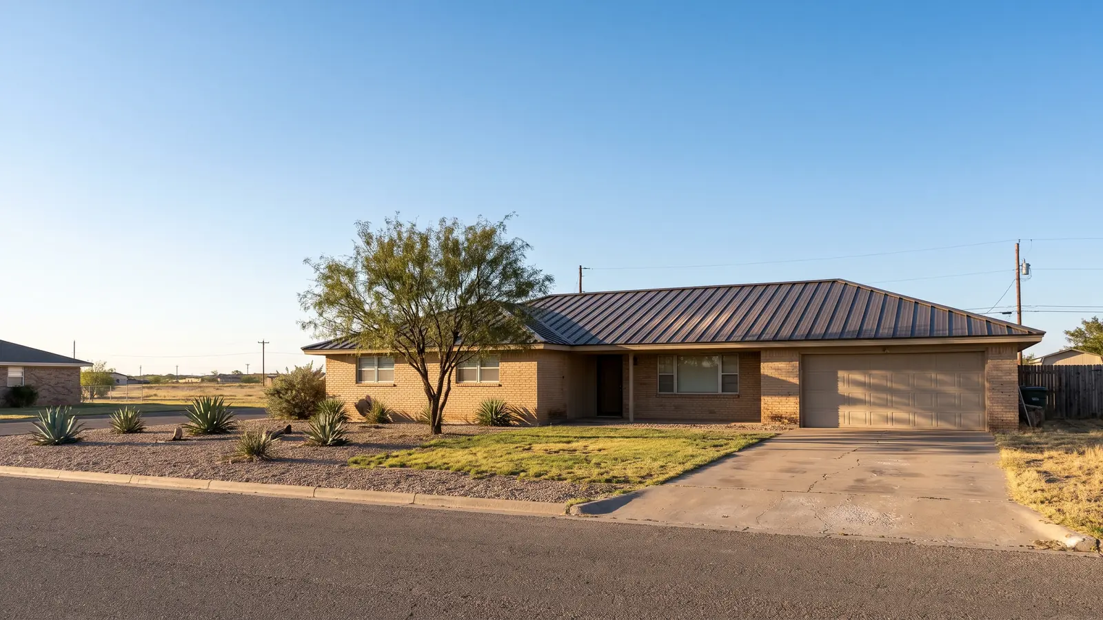 Single-story tan brick ranch house with a new dark bronze standing seam metal roof under a clear blue sky